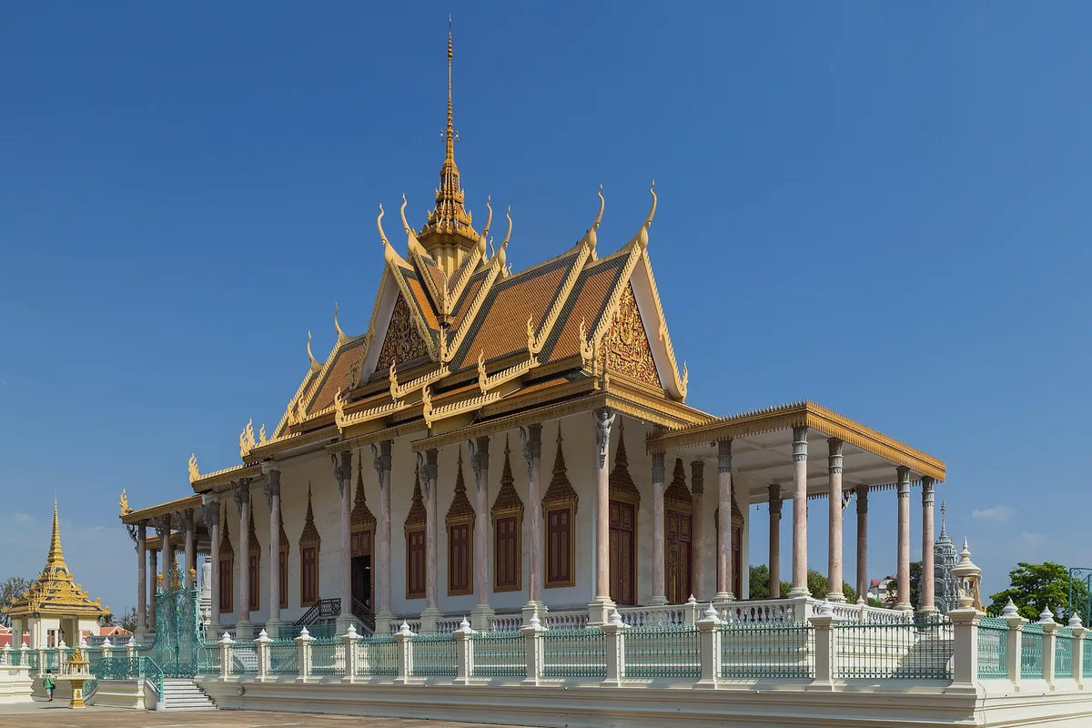 The Silver Pagoda in Phnom Penh, a white hall with golden tiered roofs and a tall spire, behind a pale blue railing.